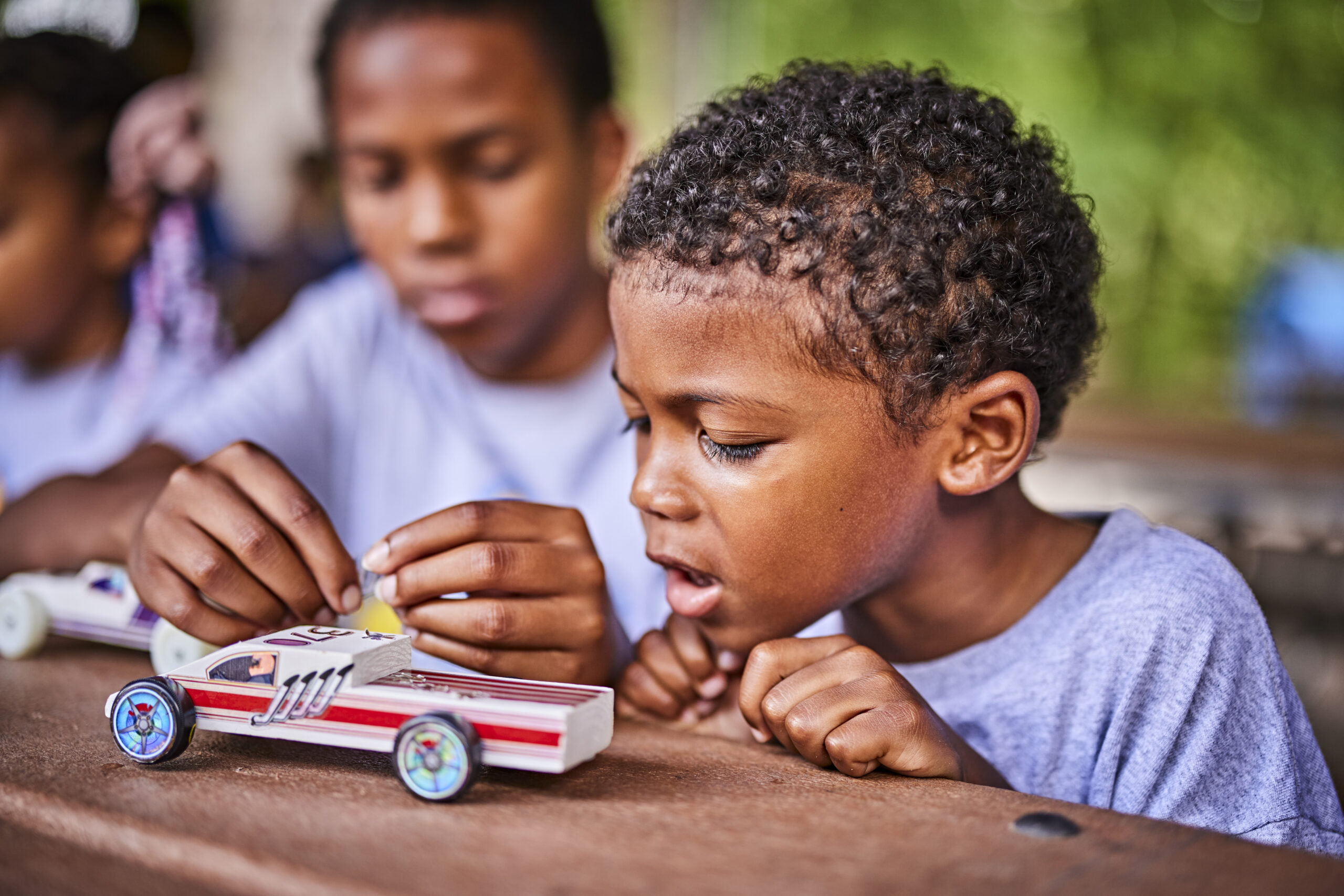 Cub Scouts building a pinewood derby car; working on a project; brothers; mentoring; putting stickers on a car